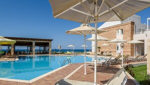 Una piscina con sillones de descanso y sombrillas, una zona de estar cubierta y vista al mar.