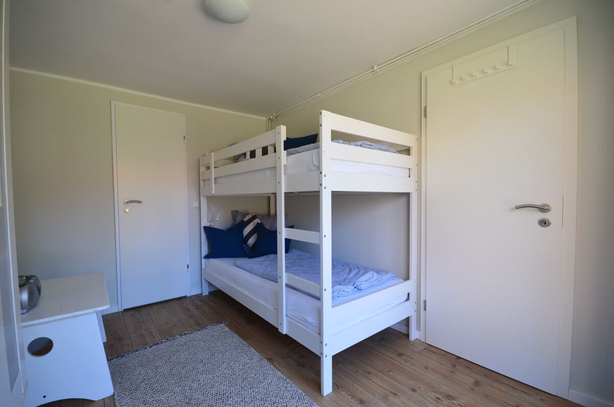 Een slaapkamer met een stapelbed, bureau en een deur.