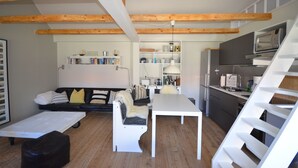 Eine moderne Küche mit Holzbalken, einem Essbereich und einem Wohnraum mit Sofa und Bücherregalen.