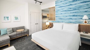 Une chambre d’hôtel avec un grand lit, un canapé, une petite table, un bureau, une lampe, une horloge et une vue sur la cuisine.