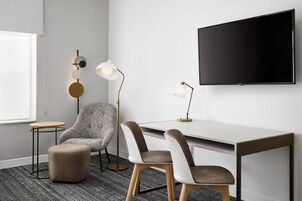 Una habitación moderna con una silla gris, dos otomanas, un escritorio y un televisor montado.
