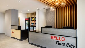 Un comptoir d’accueil avec une pancarte indiquant « BIENVENUE à Plant City », un distributeur automatique et un mur composé de lattes de bois verticales et orné d’un motif.