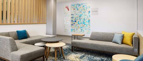 Un vestíbulo moderno con un sofá modular, mesas redondas y un gran mapa en la pared.