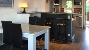 A modern kitchen with a central island, bar stools, and a dining area with a table and chairs. - MAGNIFICENT SEA VIEW 🌊  (Sausset-les-Pins)