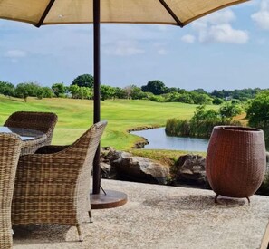An outdoor seating area with wicker furniture and a large vase, overlooking a golf course and a pond. - Villa 46 Vipingo Ridge (Vipingo)