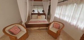 A bedroom with a bed, two wicker chairs, a bedside table, and a curtain. - Villa 46 Vipingo Ridge (Vipingo)