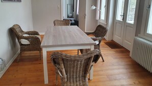 A dining area with a wooden table and wicker chairs, large windows, and a view of the outside.