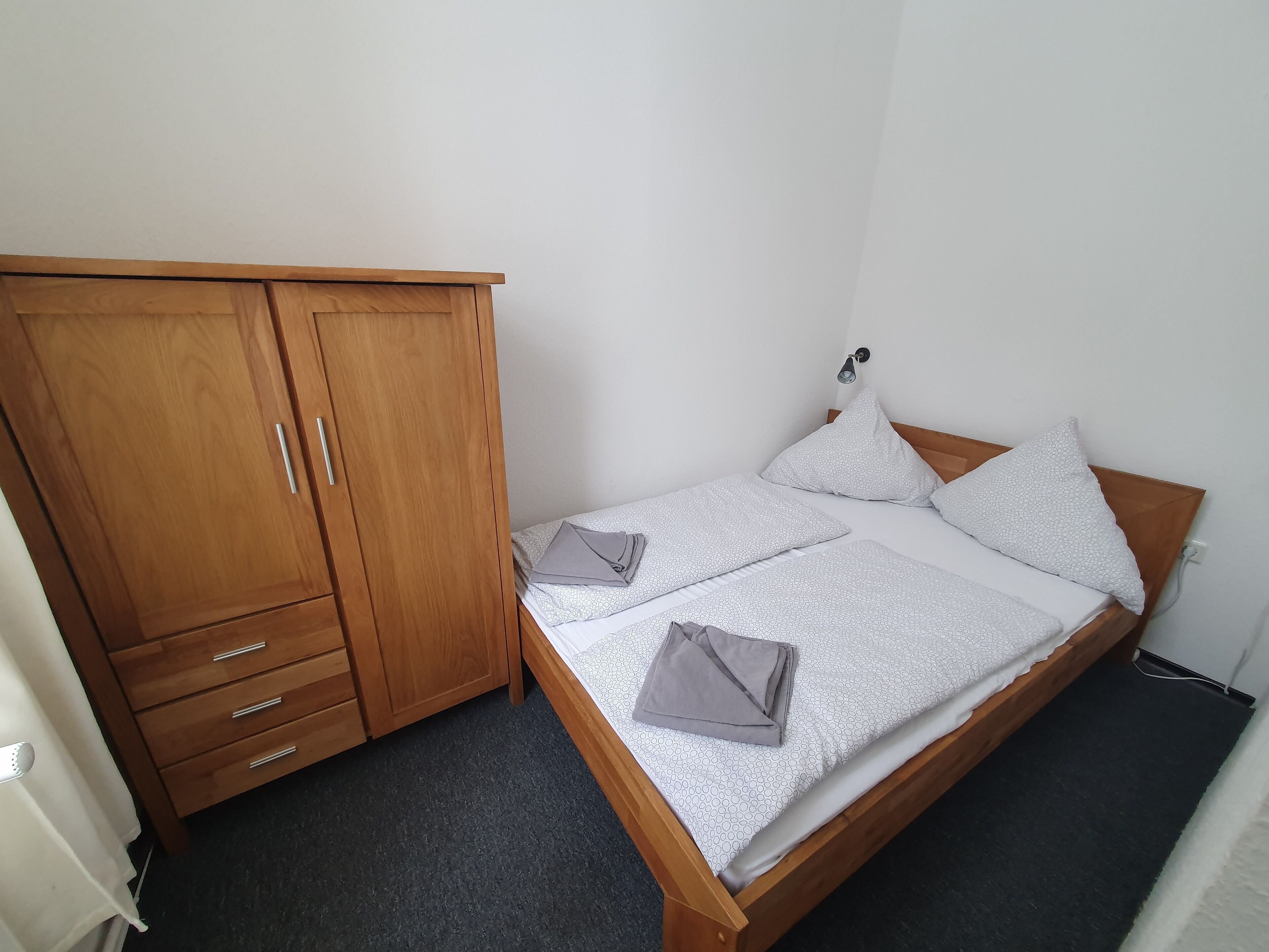Een slaapkamer met een houten bed, twee kussens, een nachtkastje en een kledingkast.
