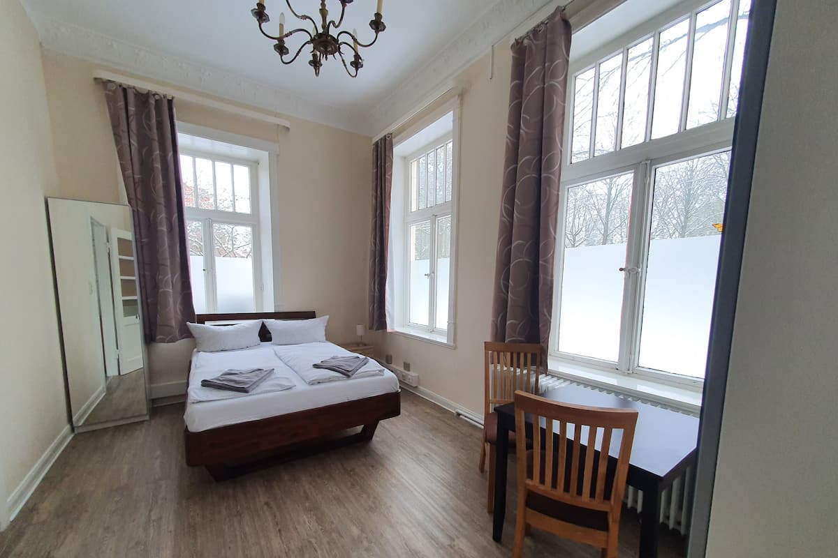 A bedroom with a bed, a chair, and large windows.