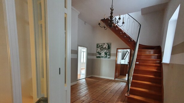 A spacious room with wooden flooring, a staircase, and a chandelier.