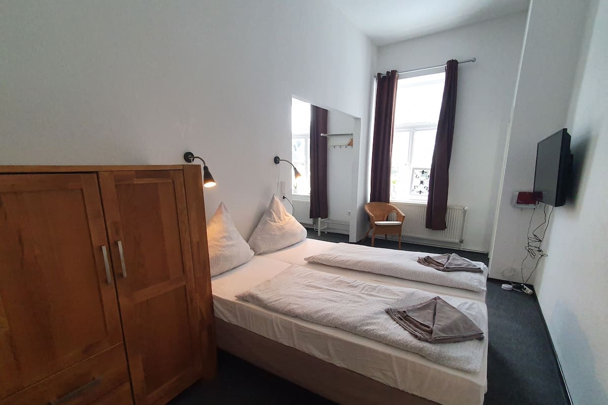 A bedroom with two beds, wooden wardrobe, and a TV on the wall.