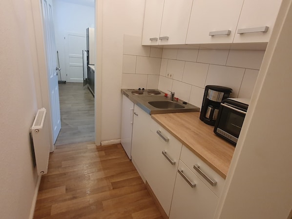 A narrow kitchen with white cabinets, a wooden countertop, a sink, and a coffee maker.