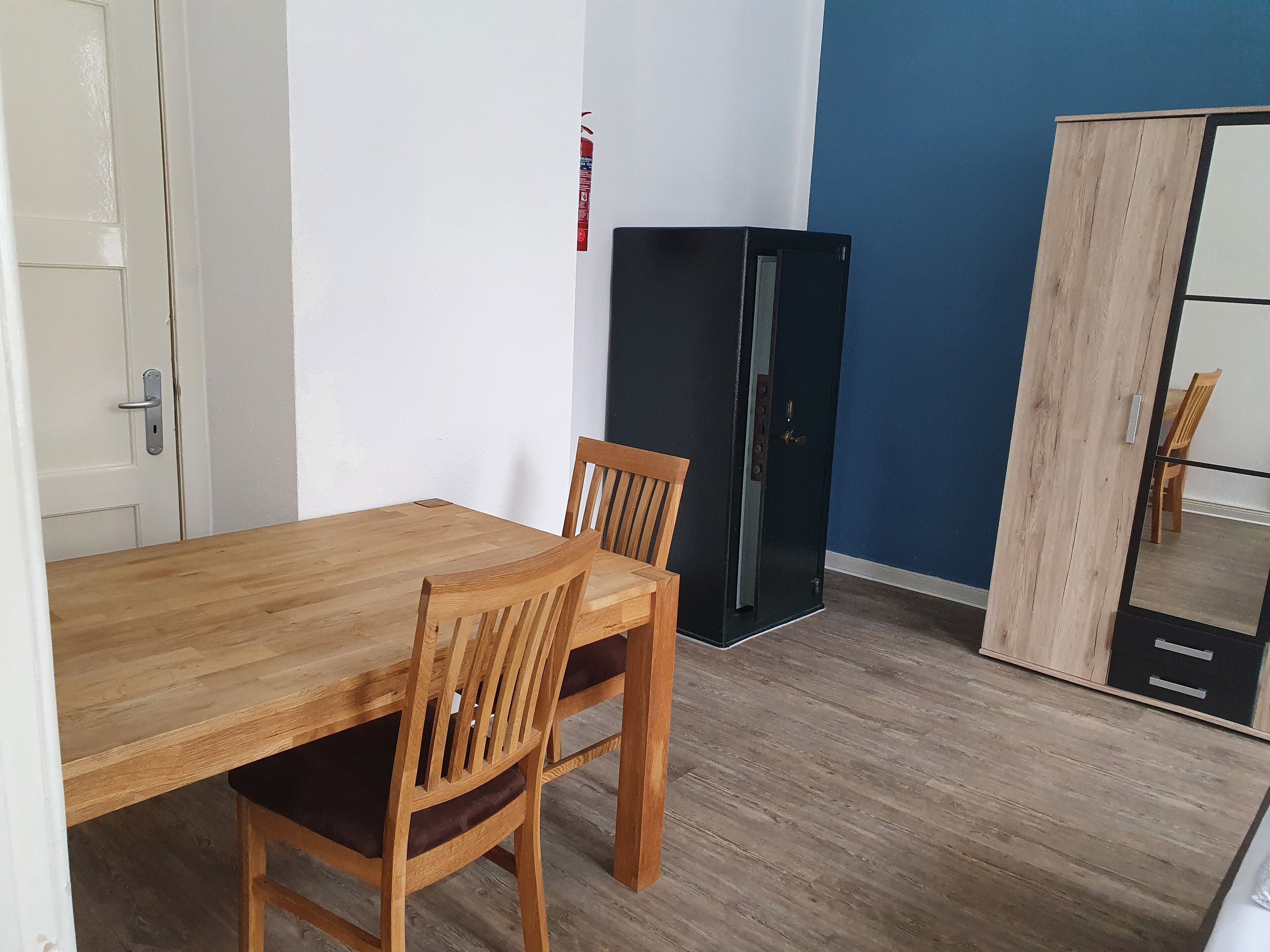 A room with a wooden dining table and chairs, a black cabinet, and a wardrobe.
