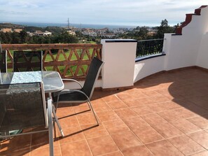 A terrace with a table and chairs, a view of the sea, and a white wall with a window. - BRIGHT PENTHOUSE SEA AND GOLF VIEWS TERRACE WIFI BARBECUE NEAR BEACH AND MARBELLA (Mijas Costa)
