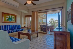 A living room with a sofa, a coffee table, and a view of a balcony with outdoor furniture.