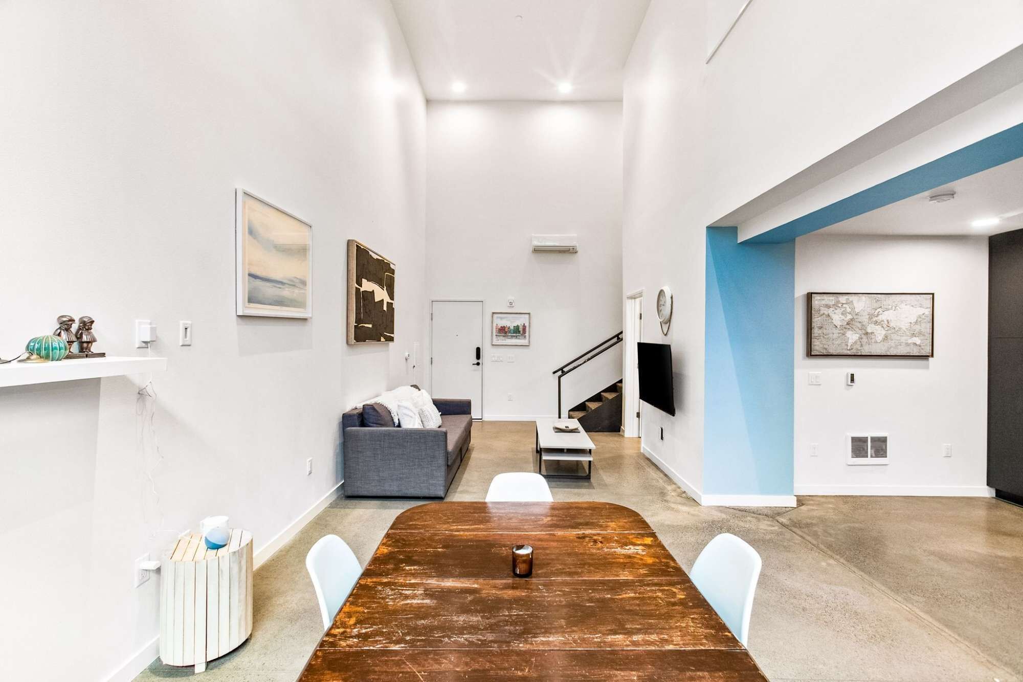 Un salon moderne avec une table à manger en bois, un canapé gris et un escalier menant à un autre niveau.