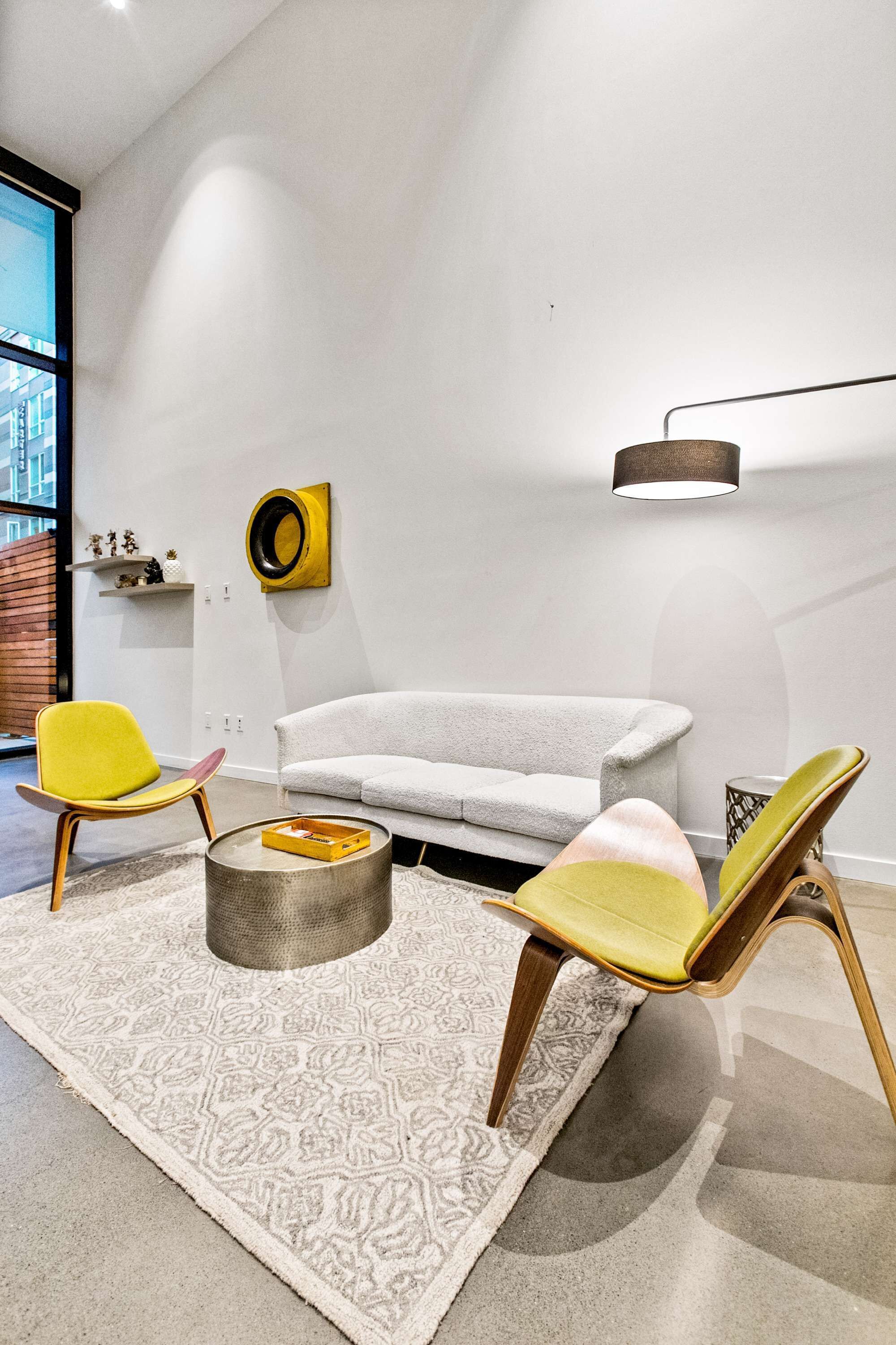 A modern living room with a grey sofa, yellow and green chairs, a round coffee table, and a minimalist decor.
