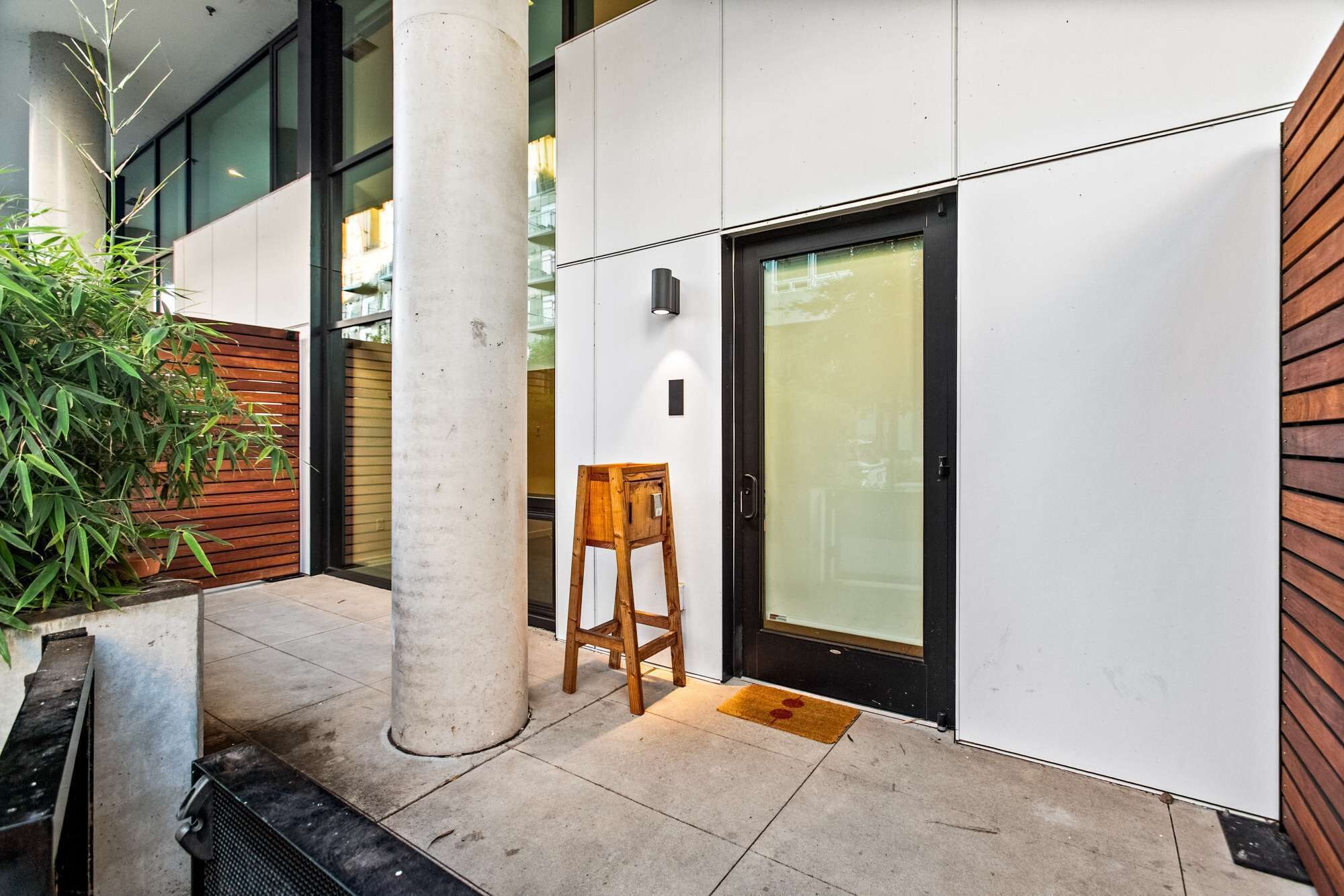 A modern building exterior with a concrete column, a wooden bench, and a glass door.