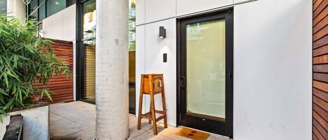 A modern building exterior with a concrete column, a wooden bench, and a glass door.