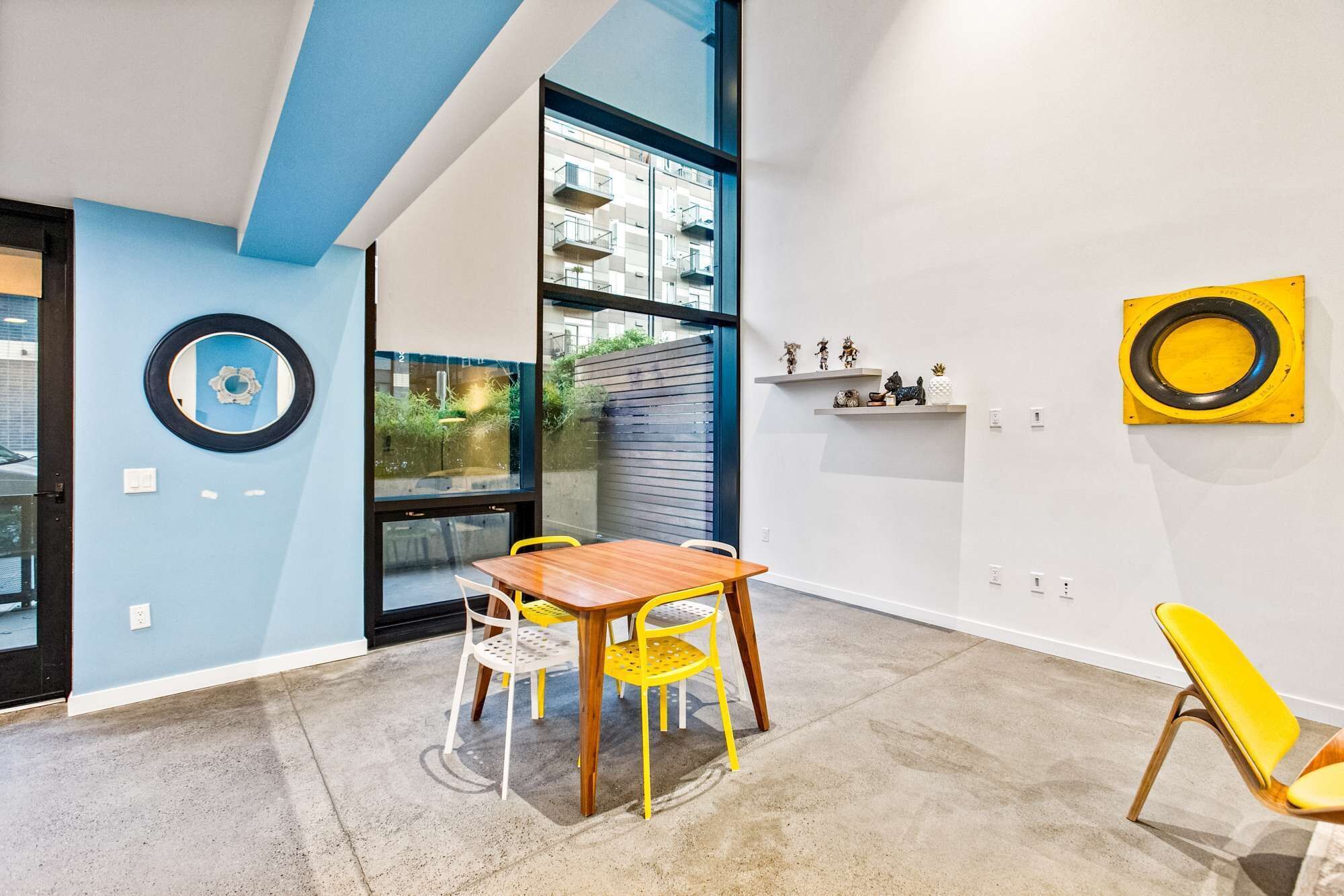 A modern interior with a wooden table and yellow chairs, a large window, and decorative items on the wall.