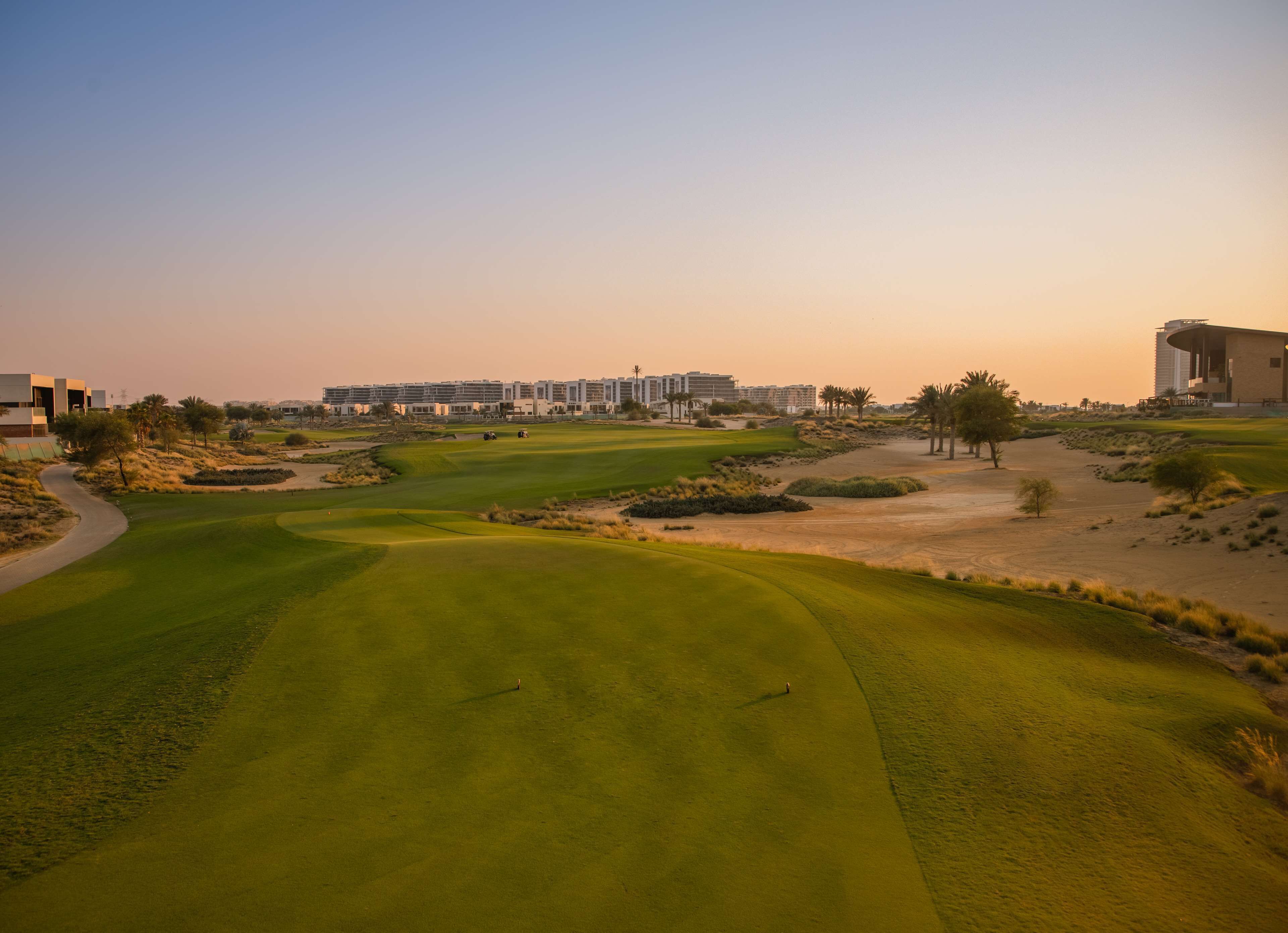 A golf course with a clear path, palm trees, and modern buildings in the background.