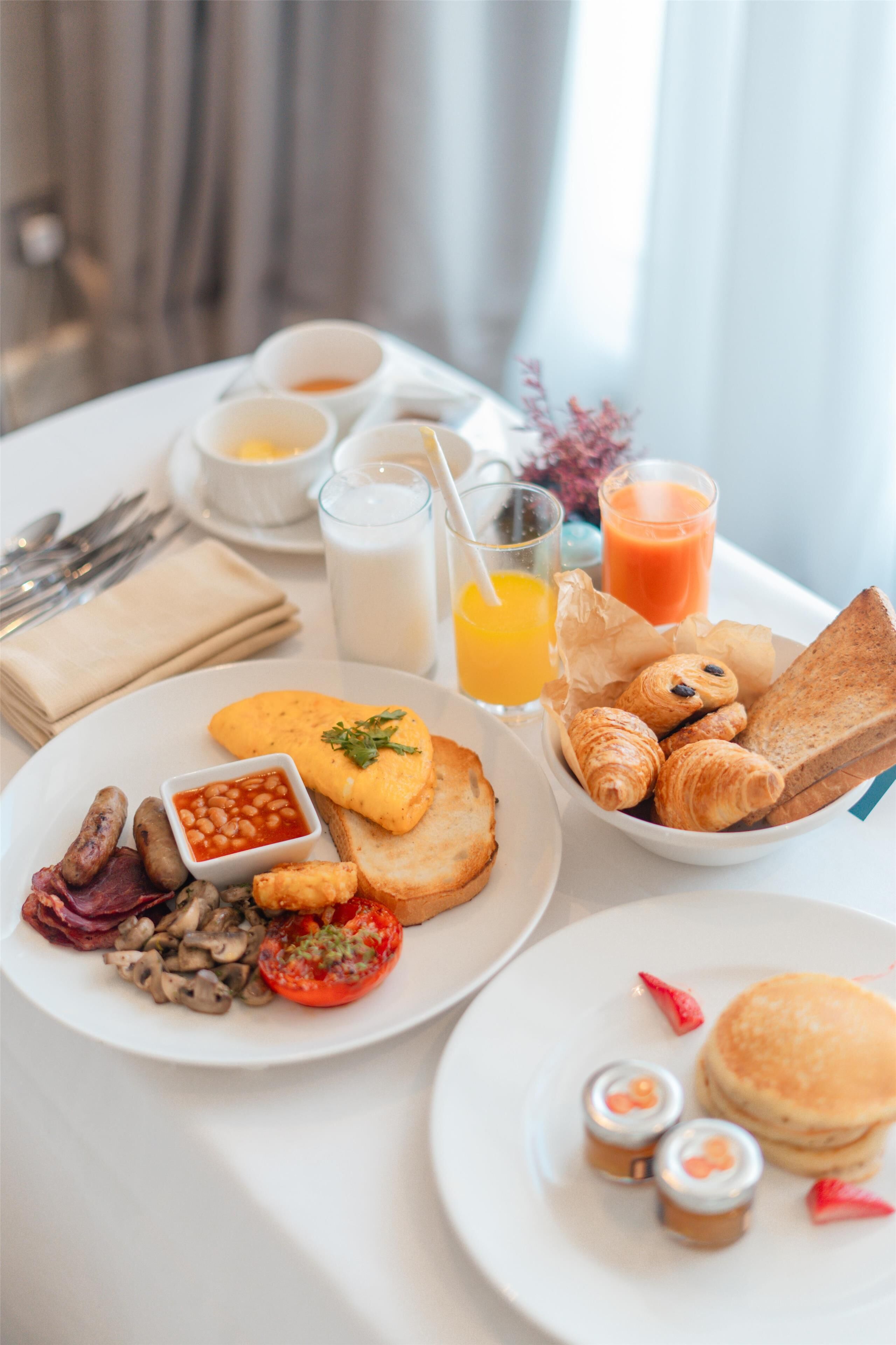Desayuno con platos de huevos, frijoles, champiñones y tostadas, además de cruasanes y panqueques.