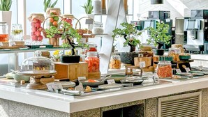 A modern buffet setup with various food items and decorative plants. - Radisson Dubai Damac Hills (Dubai)