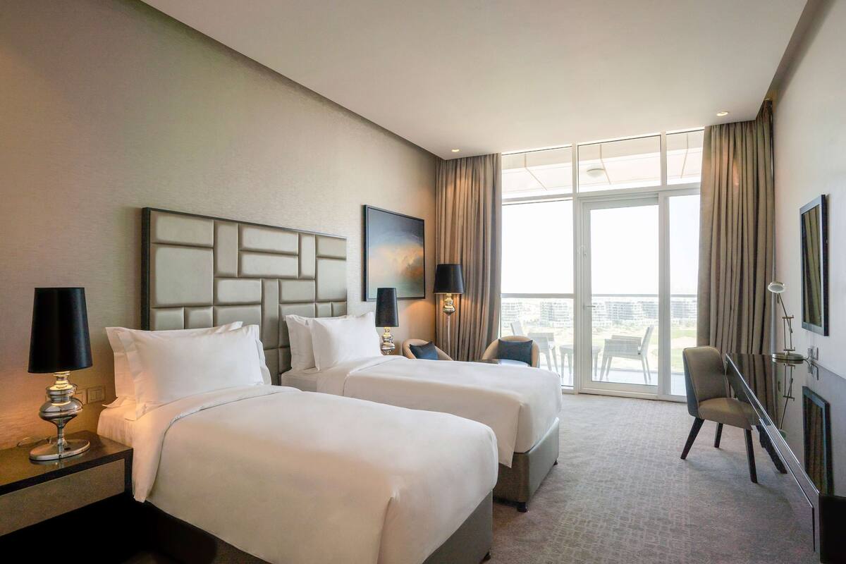 A hotel room with two beds, a large window, and a view of the city.