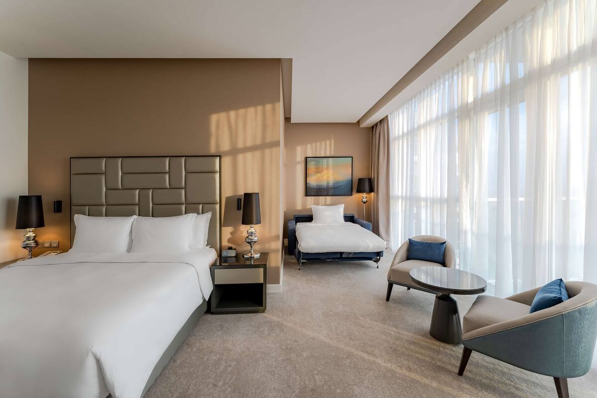 A hotel room with a large bed, a smaller bed, a sofa, a coffee table, and a painting on the wall.