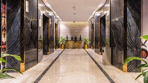 A modern hotel lobby with marble flooring, elevators, and a reception desk with decorative vases and plants. - Radisson Dubai Damac Hills (Dubai)