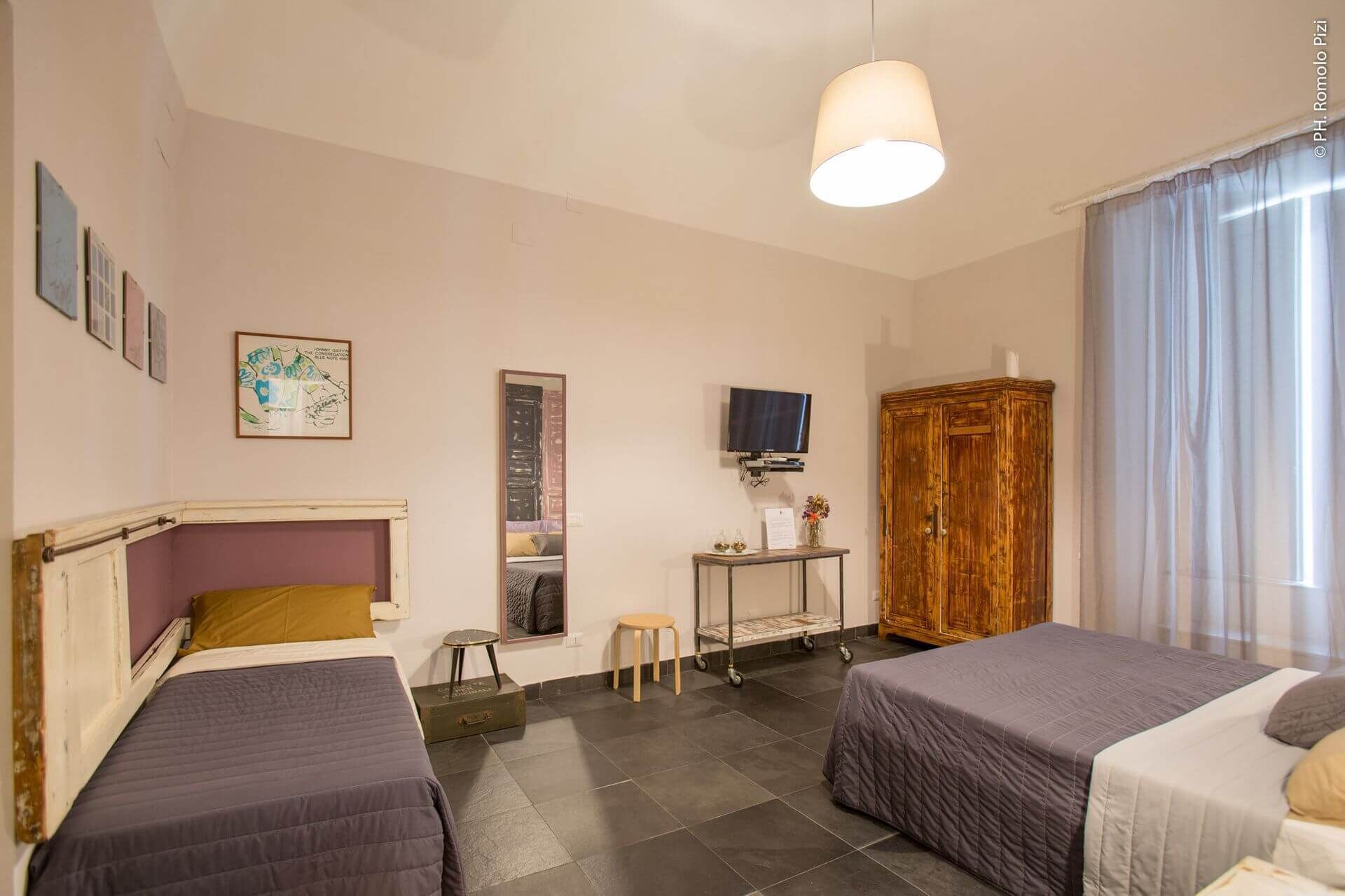 A hotel room with two beds, a television, a small table with a mirror, and a wooden wardrobe.