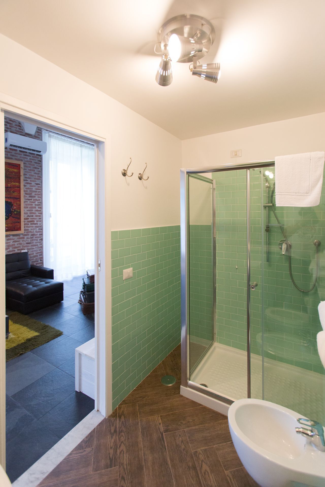A modern bathroom with a glass shower enclosure, a white sink, and a green-tiled shower wall.