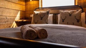 A wooden cabin room with a bed, two pillows with deer head prints, and a rolled towel on the bed. - Luxury Safari Lodge-sleeps 4/6-deer Park-dogs Ok (Crediton)