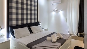 Una camera d'albergo moderna con una testiera a scacchi, un letto rifatto con asciugamani, un condizionatore d'aria a parete e un angolo doccia con tenda.