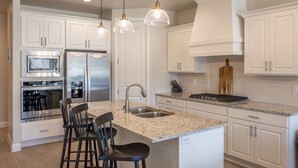 A modern kitchen with white cabinets, stainless steel appliances, a granite countertop, and bar stools.