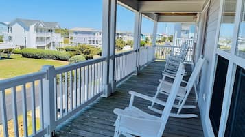 A covered porch with white rocking chairs, a wooden deck, and a view of neighboring houses.