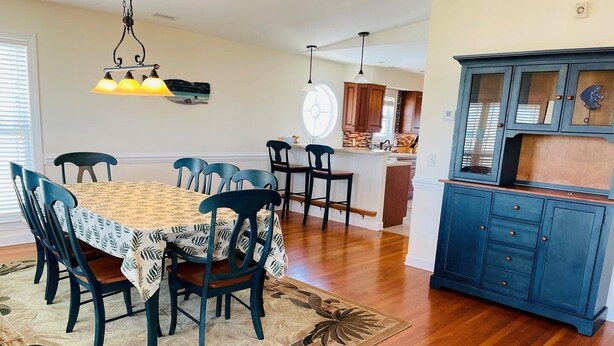 A dining area with a table, chairs, a rug, a hanging light fixture, and a kitchen area with cabinets. - Holden' A Full House 4 Bedroom Home by RedAwning (Supply)