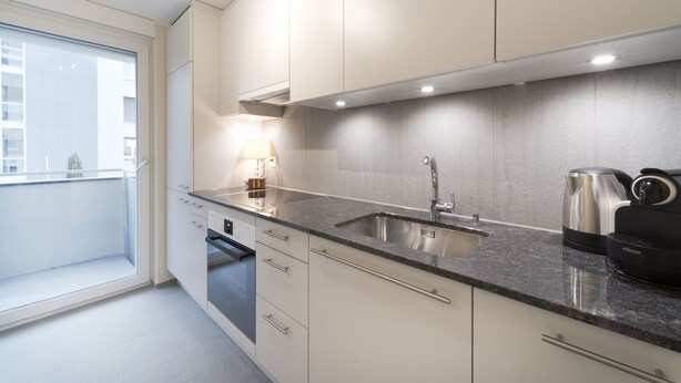 A modern kitchen with a built-in sink, a coffee machine, and a window overlooking a cityscape. - RELOC Serviced Apartments Wallisellen 36 (Wallisellen)