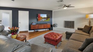 A modern living room with a grey sofa, a red ottoman, a wooden coffee table, and a TV mounted on the wall. - 3/2 10 min Downtown Near Restaurants, Pet-Friendly (Austin)