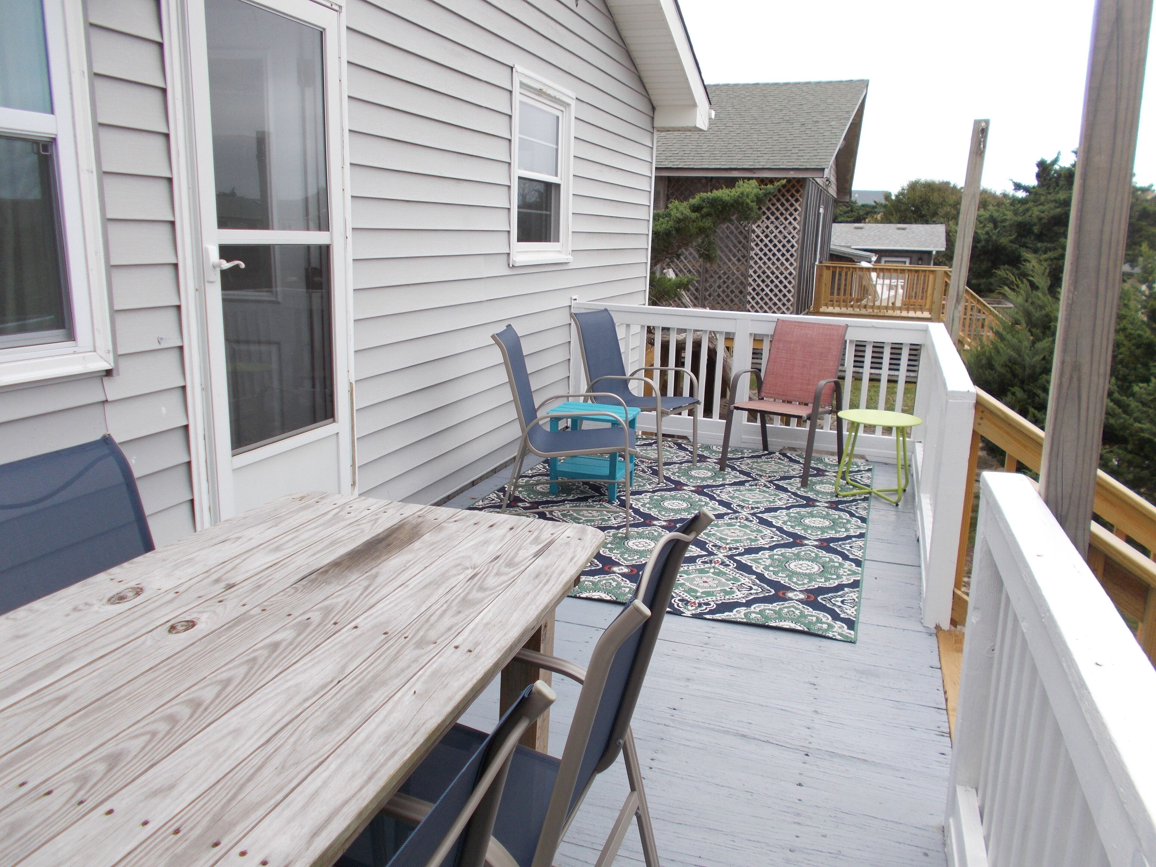 A wooden deck with a table and chairs, a small table with a green top, and a patterned rug.