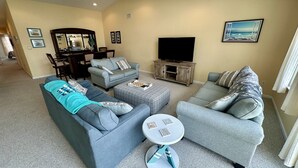 A living room with two grey sofas, a coffee table, a TV stand, and a dining area with chairs and a table.