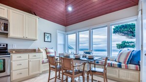 A kitchen with wooden cabinets, a dining table set for four, and a view of the ocean through large windows.
