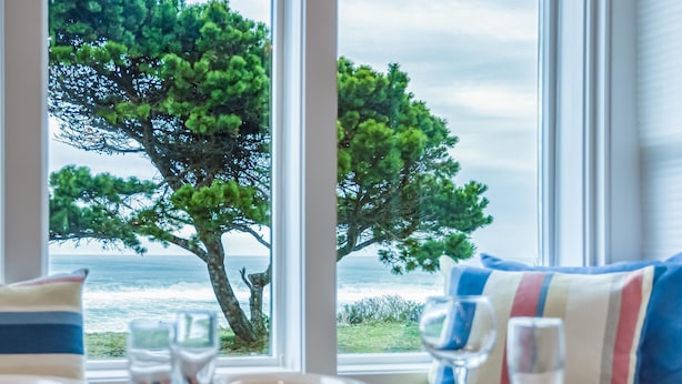 A dining table with plates and glasses, a striped pillow, and a view of the ocean through a window with a tree.