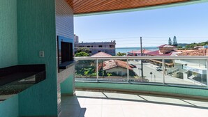 A balcony with a view of the sea and buildings, a tiled wall, and a wooden ceiling. - Zancanaro Apto 202  641D (Bombinhas)