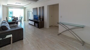A modern living room with a sofa, a glass coffee table, a flat-screen TV, and a dining area with chairs and a table. - Zancanaro Apto 202  641D (Bombinhas)