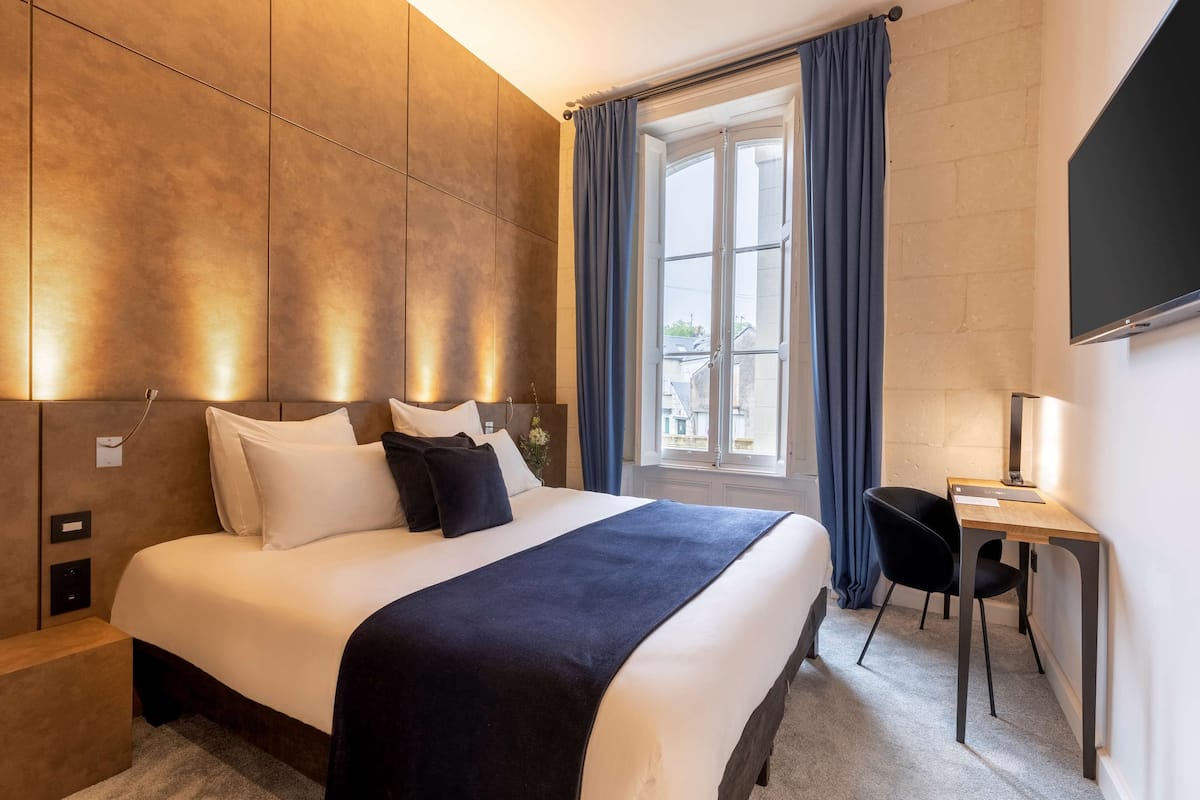 A modern hotel room with a large bed, a desk, and a window with curtains.