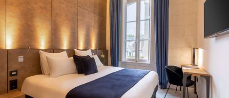 Een moderne hotelkamer met een groot bed, een bureau en een raam met gordijnen.