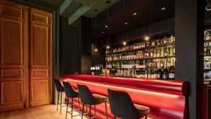 A bar area with a red countertop, wooden cabinets, and black bar stools.