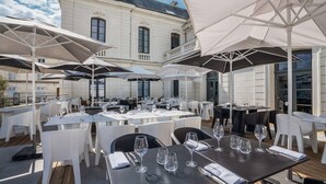 An outdoor dining area with tables and chairs, umbrellas, and a building in the background.