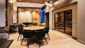 A modern restaurant with a round table set for dining, wooden paneling on the walls, and a wine rack visible through the glass door.